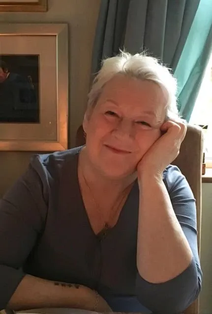 Sue Cox smiling warmly, resting her chin on her hand