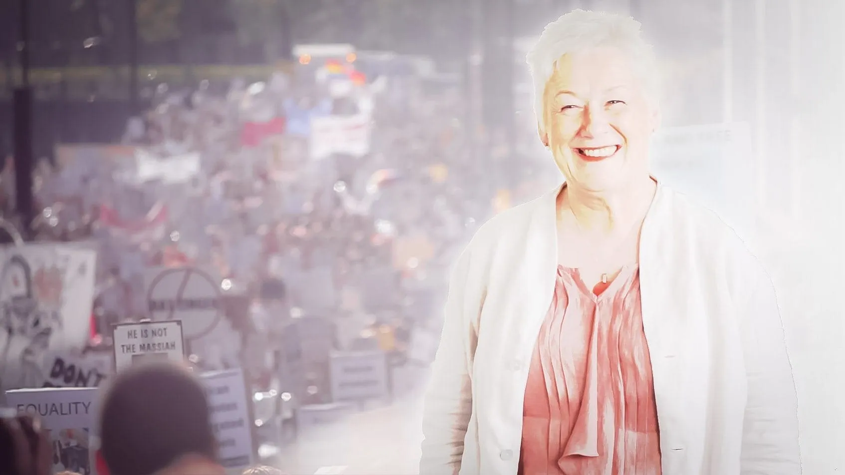 Sue Cox smiling, with the crowd of the Protest the Pope march behind her
